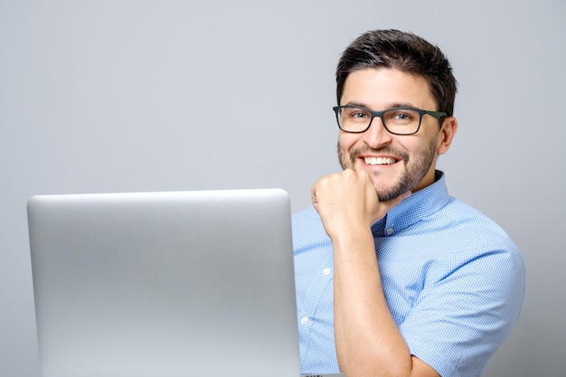 Портрет молодого улыбающегося мужчины, сидящего за столом с ноутбуком