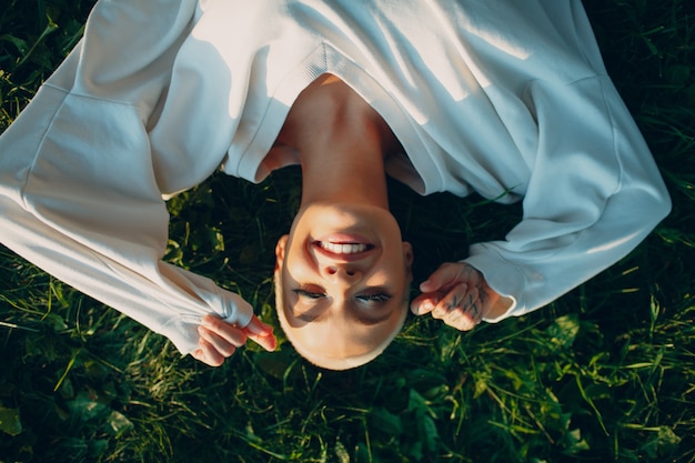 Photo portrait of young smiling millenial european short haired woman teenager lies on green grass meadow ...