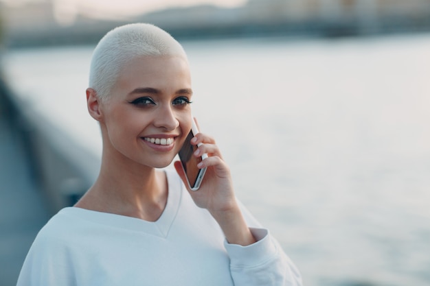 Portrait of young smiling millenial european short haired woman using mobile phone beautiful happy b...