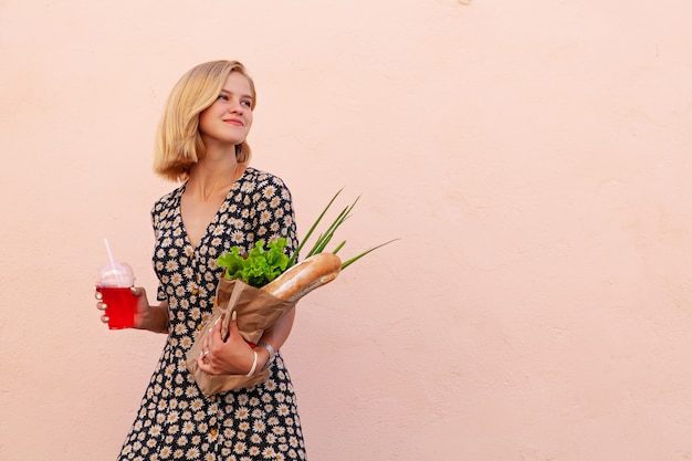 Portrait of young smiling student woman with craft shop bag, with green salad, onion and bread. Healthy food, snack