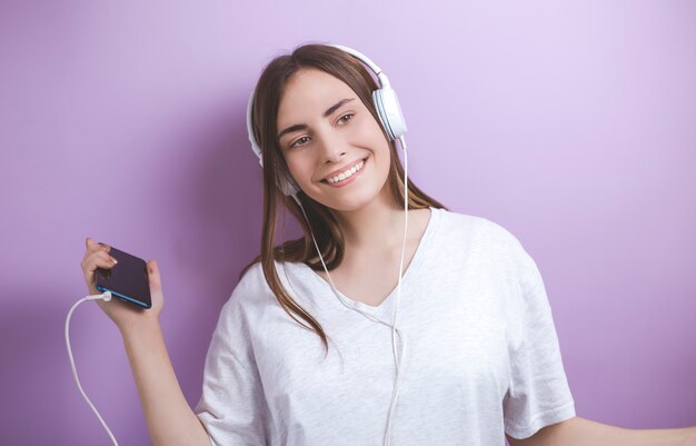 Portrait of a young smiling woman dancing listening to music in headphones from a smartphone. 