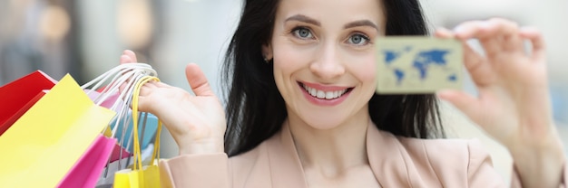 Portrait of young smiling woman holding credit bank card and shopping bags in hand