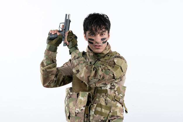 Portrait of young soldier in camouflage with gun on white wall