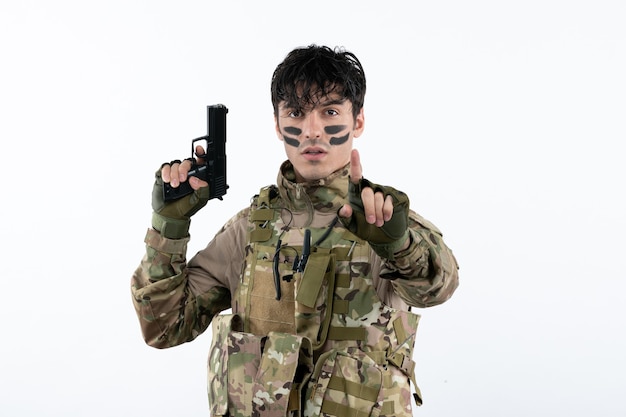 Photo portrait of young soldier in camouflage with gun on white wall