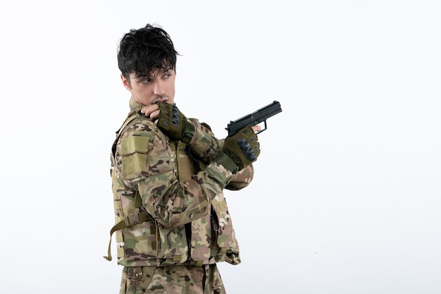 Photo portrait of young soldier in camouflage with gun on white wall