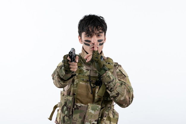 Portrait of young soldier in camouflage with gun on white wall