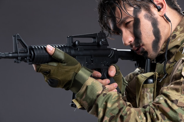 Portrait of young soldier in camouflage with machine gun on the dark wall