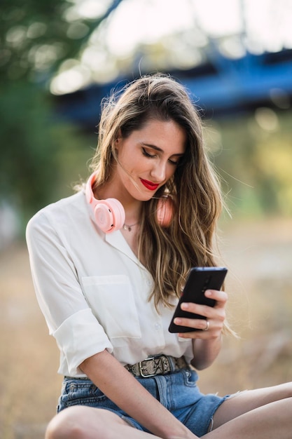 Portrait of a young Spanish woman with hair highlights sitting in a park and texting on her phone