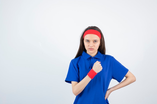 Portrait of a young sporty girl showing fist on a white wall