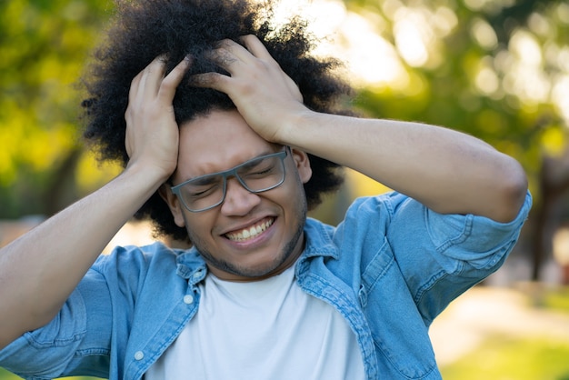 Portrait of young stressed man suffering headache outdoors on the street.