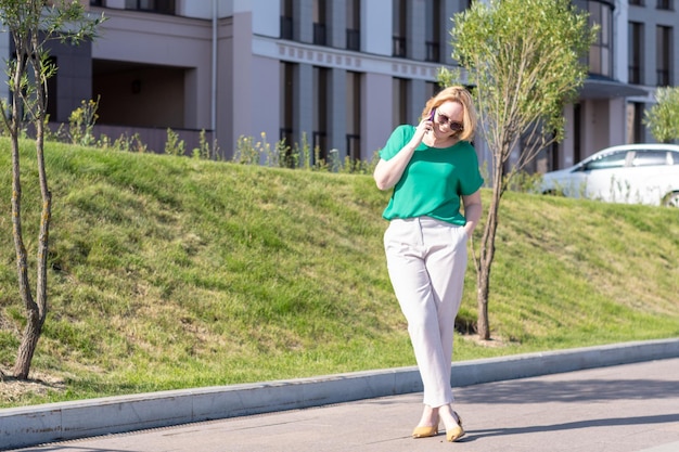 Portrait of young student girl in glasses standing outdoors and talking on cell phone