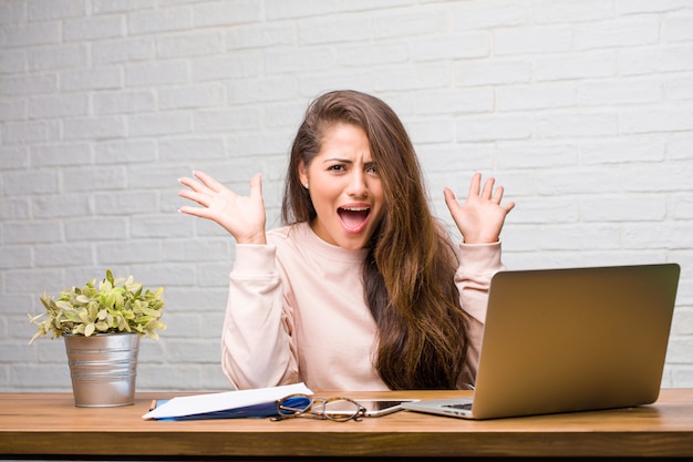 Portrait of young student latin woman sitting on her desk crazy and desperate