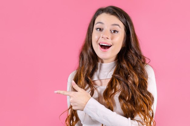 A portrait of a young student pointed by finger on copy space with pink background