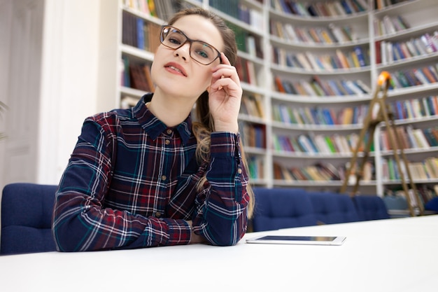 Photo portrait of a young student woman in glasses who is sitting in the public library