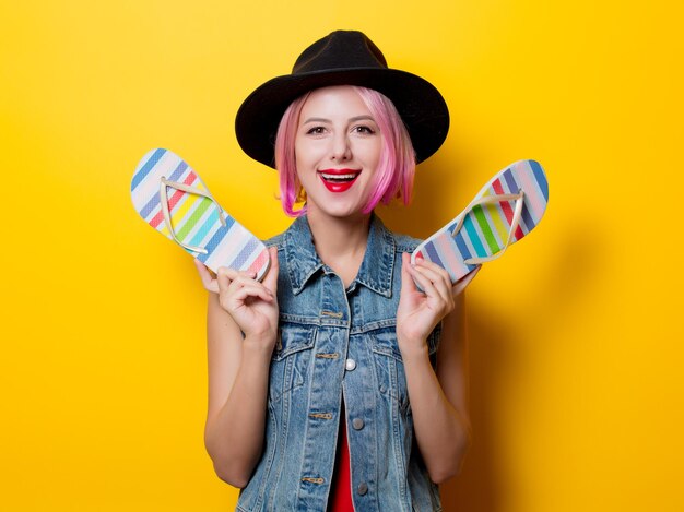 Portrait of young style hipster girl with pink hairstyle and flip flops shoes on yellow background