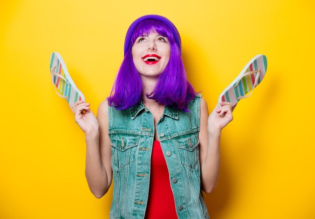 Portrait of young style hipster girl with purple hairstyle with flip flops shoes on yellow background