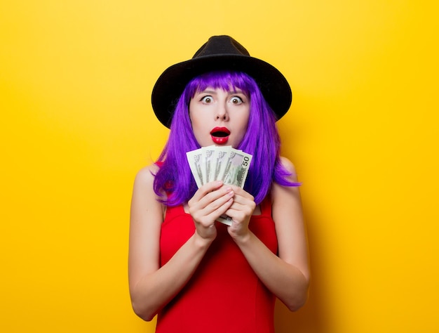 Portrait of young style hipster girl with purple hairstyle with money on yellow background