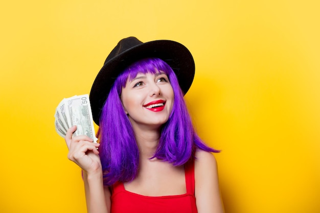 黄色の背景にお金と紫色の髪型の若いスタイルの流行に敏感な女の子の肖像画