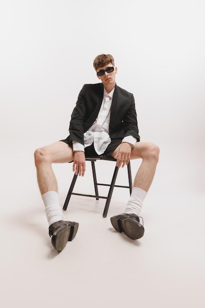 Portrait of young stylish man sitting on chair posing isolated over white studio background