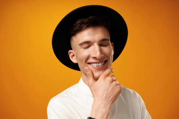 Portrait of a young stylish man wearing black hat against yellow background
