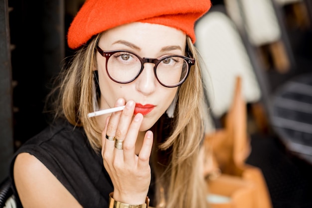 Photo portrait of a young stylish woman in red beret and eyeglasses smoking a cigarette