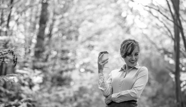 Portrait of young stylish woman with coffee on the autumn park background Breakfast on the go warming up concept Black and white photo