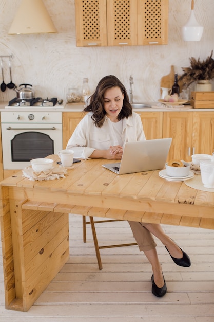 Портрет молодой успешной кавказской женщины-фрилансера сидит за столом у себя дома, уверенная женщина работает онлайн на ноутбуке дома
