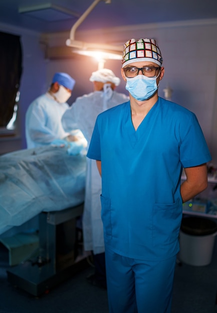 Foto ritratto di giovane medico chirurgo in camice in piedi in sala operatoria. ritratto di medico maschio nella moderna sala medica.