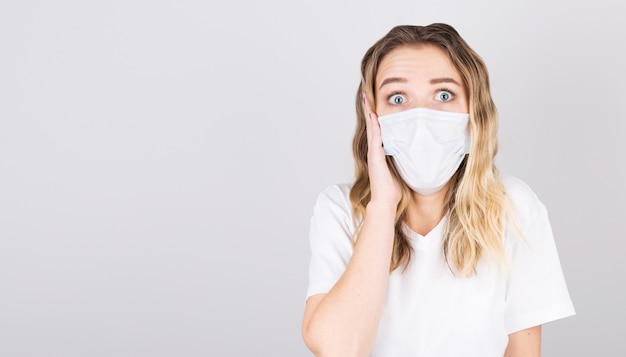 Portrait of a young surprised woman in a medical mask isolated over grey background