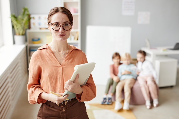 Portrait of young teacher in eyeglasses holding her report looking at camera while standing in the c...