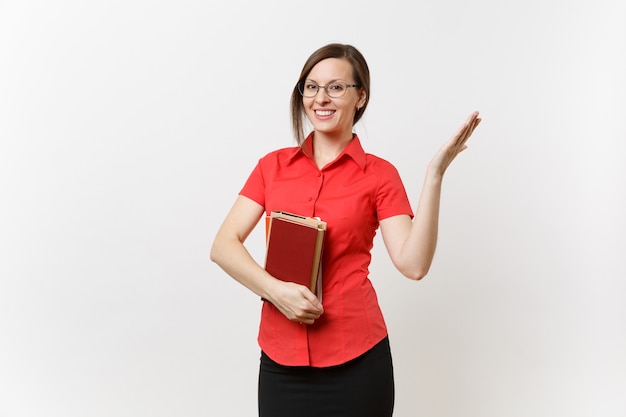 Портрет молодой женщины учителя в красной рубашке, юбке и очках, держа книги, указывая рукой в сторону на космосе экземпляра, изолированном на белой предпосылке. Образование или преподавание в концепции университета средней школы.