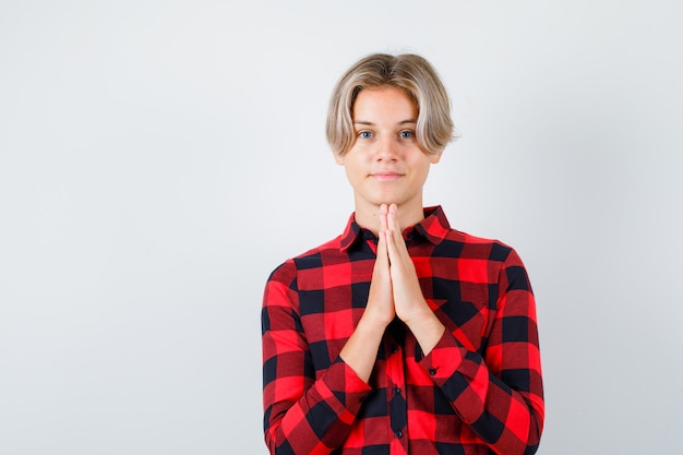 Portrait of young teen boy keeping hands in praying gesture in checked shirt and looking thankful front view