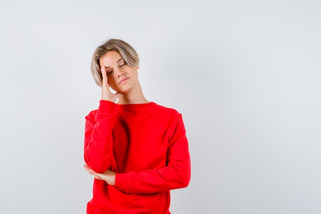 Portrait of young teen boy leaning head on hand in red sweater and looking tired front view