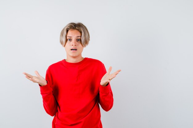 Portrait of young teen boy showing helpless gesture in red sweater and looking puzzled front view