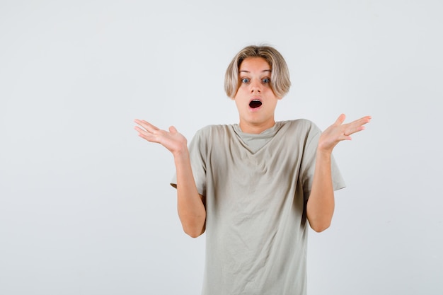 Portrait of young teen boy showing helpless gesture in t-shirt and looking surprised front view