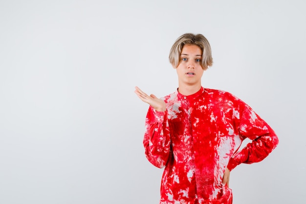 Portrait of young teen boy spreading palm aside in shirt and looking scared front view