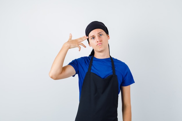 Portrait of young teen cook showing suicide gesture in t-shirt, apron and looking depressed front view