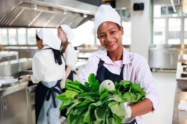 Ritratto giovane ragazza adolescente cuoco studente classe di cucina culinaria aula felice giovane donna africana studenti in possesso di verdure fresche per cucinare nella scuola di cucina