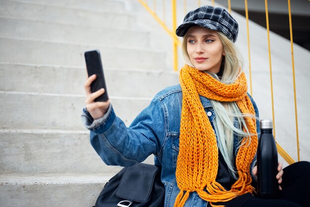 Portrait of young teenage blonde girl, taking selfie photo with smartphone