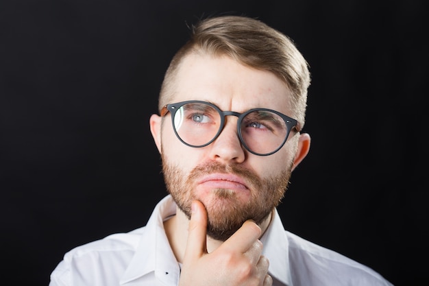 Portrait of young thoughtful bearded man and in glasses over the black background