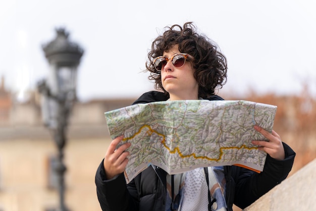 Portrait of a young tourist woman with curly hair searches for\
a place in the city with the help of a map
