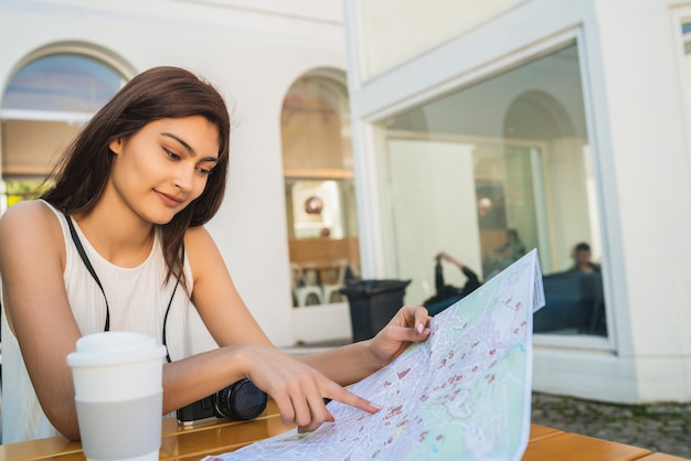 地図とコーヒーショップに座って道順を探している若い観光客の女性の肖像画。旅行のコンセプト。