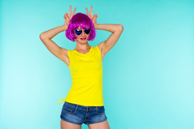 Portrait of young transgender woman with problem skin in pink wig and sunglasses heart shape on blue background