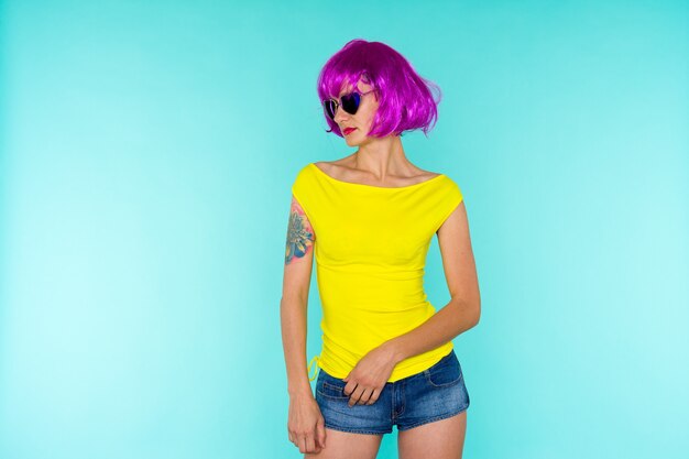 Portrait of young transgender woman with problem skin in pink wig and sunglasses heart shape on blue background