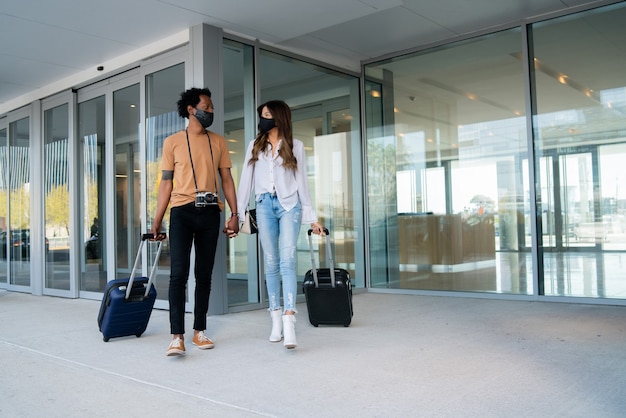 Portrait of young traveler couple wearing protective mask and carrying suitcase