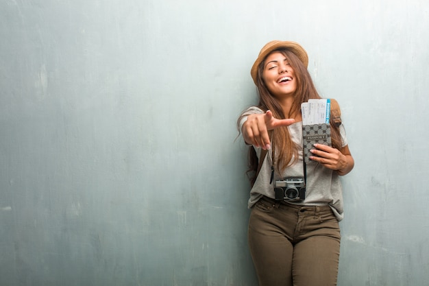 Portrait of young traveler latin woman against a wall shouting, laughing and making fun of another