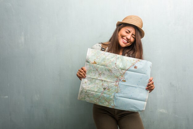 Ritratto di giovane donna latina viaggiatore contro un muro molto felice ed emozionato, alzando le braccia, celebrando una vittoria o successo, vincendo la lotteria. in possesso di una mappa della città.