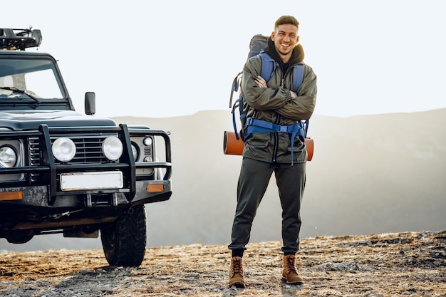 Portrait of a young traveler man in hiking equipment standing near his off-road car