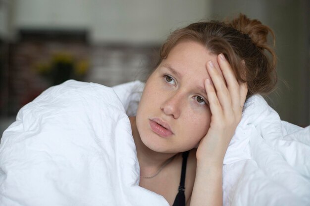 Portrait of young unhappy depressed girl beautiful lazy lonely woman covering herself in blanket suffering from depression with sad upset frustrated look at home in living room in early morning