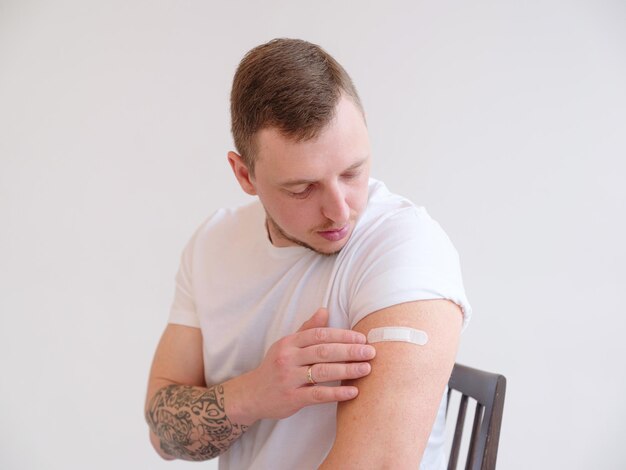 Portrait of young vaccinated man with coronavirus vaccine plaster on his shoulder